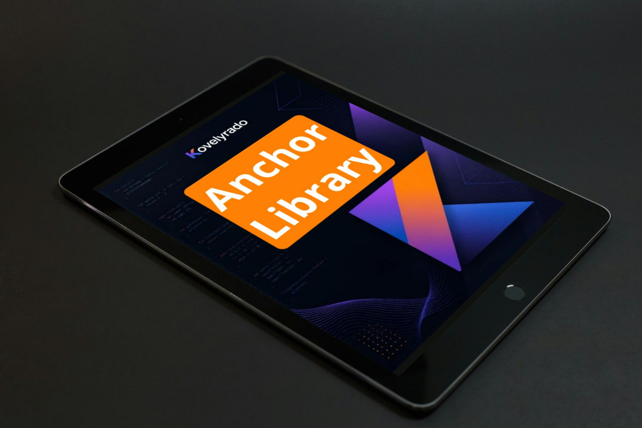 A black tablet device shown at an angle on a dark surface, displaying a colorful screen with the text 'Koyepiso' and a large orange badge reading 'Anchor Library'.