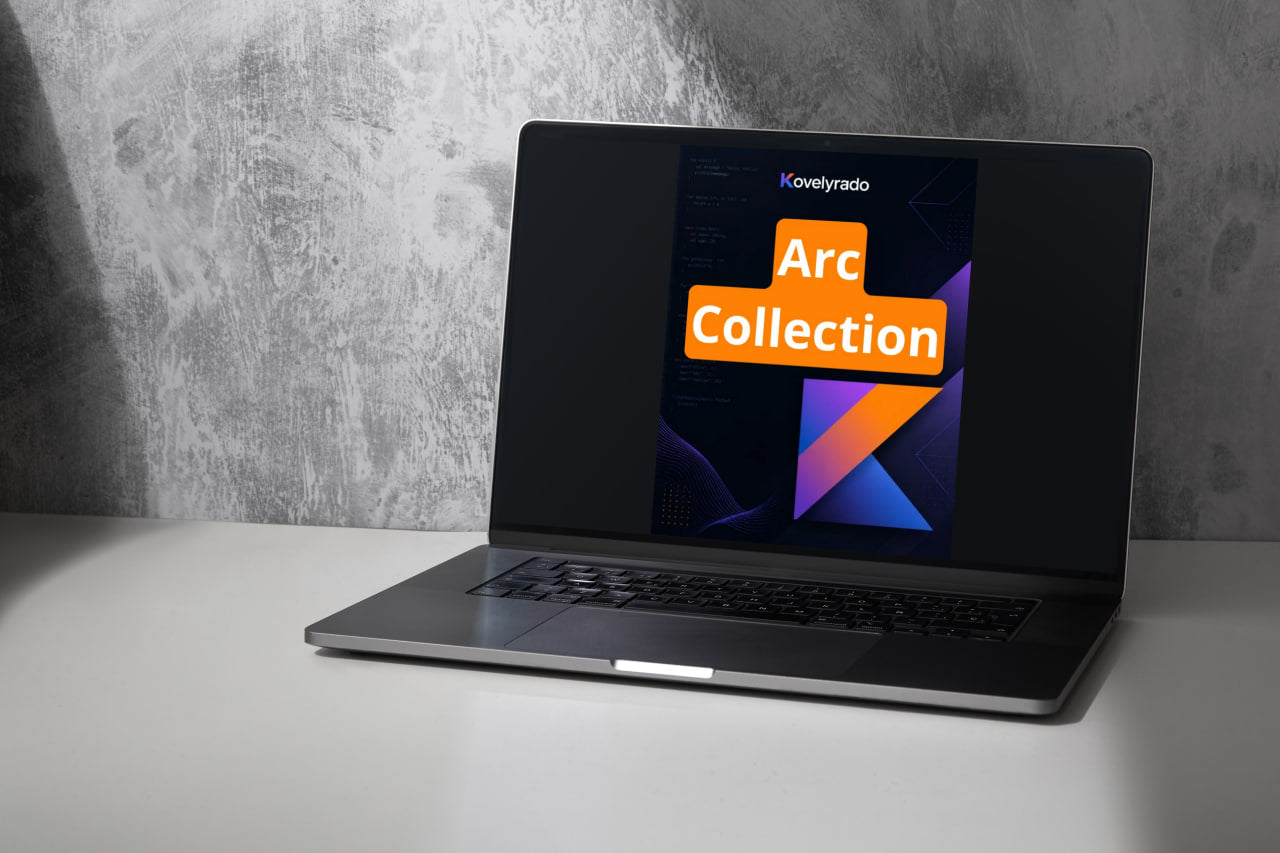 A silver laptop sits open on a white tabletop against a textured gray wall. The screen displays a graphic with the text 'Kovelrado' and 'Arc Collection' in orange and white over a dark abstract background.