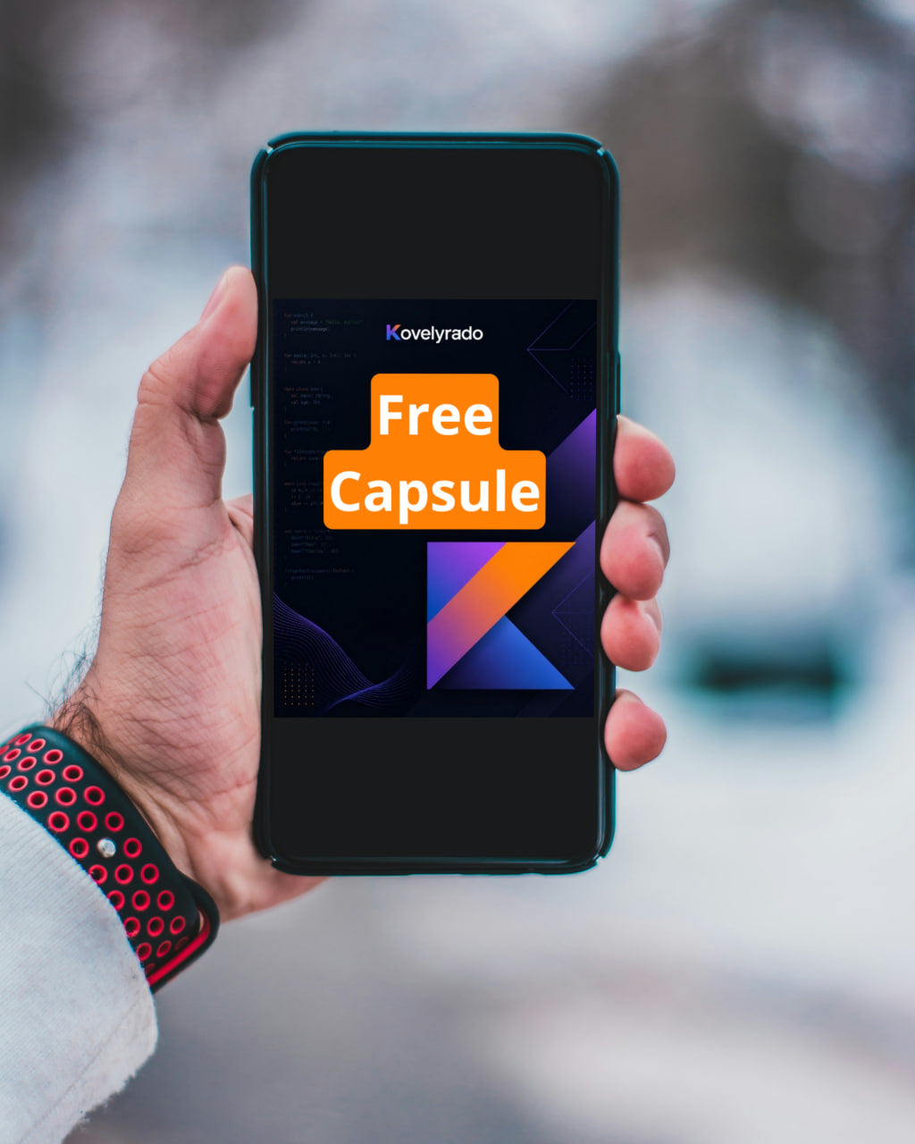 A hand holding a smartphone that displays the Kovyrlado Free Capsule offer against a blurred outdoor winter background.